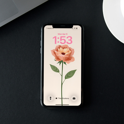 Smartphone with a floral screen on a dark surface next to a laptop and coffee cup.